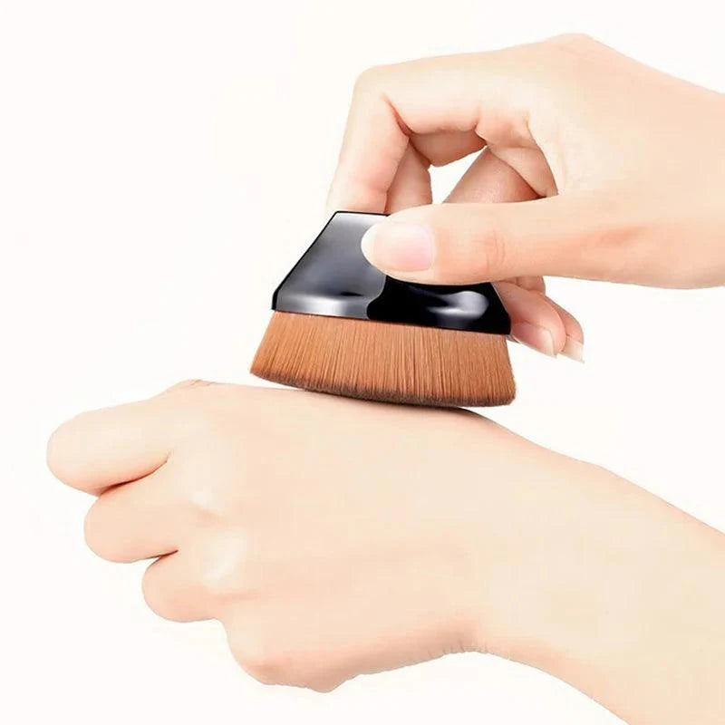 Hand using a petal-shaped flat top kabuki brush for foundation application on skin. Ideal for liquid and cream cosmetics.